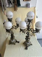 Pair of vintage bronze and marble table lamps with cherub figures, ornate arms holding frosted glass globes with gold floral patterns and hanging clear glass droplets. One lamp is missing one globe.
