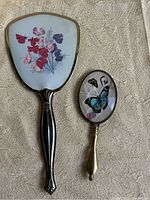 Front view of the two mirrors showing decorative backs, floral and butterfly prints.