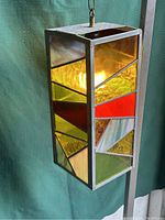 View of the vintage stained glass swag lamp showing colorful geometric pattern on side with lit bulb inside, highlighting red, yellow, green textured glass panels.