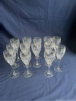 Thirteen Noritake crystal water goblets and wine glasses arranged in rows on a blue fabric background, showing their cut crystal pattern and clear glass quality.