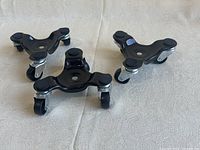 Three black triangular wheel mover dollies arranged on a fabric surface showing wheels and top padding.