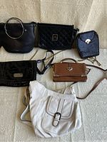 Lot of 6 women’s bags displayed on a beige textured surface; includes a variety of black, tan, and cream bags in different shapes and materials as described.