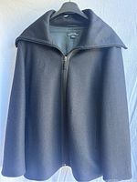 Front view of black women's jacket hanging on a black hanger against a plain background showing zip closure and large fold-over collar.