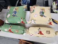 Overhead view of two square pillows and two cylindrical bolster pillows, showing Alice in Wonderland character designs on cream and green fabric backgrounds.