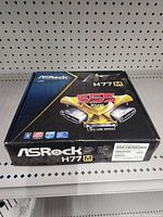 Closed box showing ASRock H77M branding and key features like 5x USB speed and compatibility with Intel and ATI.