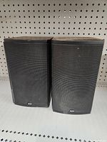 Pair of black Boston speakers side by side; left speaker cover bent, right intact, showing overall condition.
