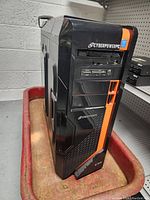 Front and side view of CyberPowerPC CFI computer case showing black and orange design, front panel with drive bays, ventilation, and ports.
