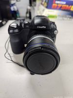 Front view of Fujifilm FinePix S5000 digital camera with lens cap attached.