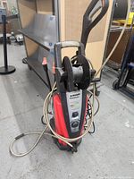 Full front view of the red and black Husky Powerwasher upright with hose and reel showing the overall condition and attached hose.