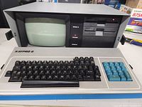 Front view of Kaypro II showing built-in CRT monitor, keyboard with black and blue keys, and dual floppy disk drives.