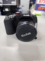 Front view of black Kodak digital camera with lens cap on the lens.