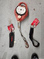 Photo showing Miller retractable lifeline with two Husky carabiner hang straps laid on gray floor.