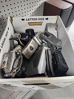 Box filled with various cameras including reflex camera, compact digital cameras, and camcorders in different conditions.