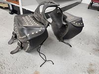 Photo showing front and side views of the two black leather motorcycle saddle bags with stud embellishments and central connecting panel.
