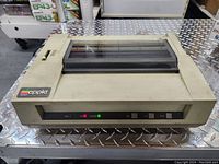 Front view of vintage Apple dot matrix printer showing the control panel with buttons and indicator lights. The printer shows signs of age and discoloration.