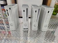 Front view of four white Xbox 360 consoles showing disc drives and power buttons.