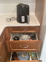 Hamilton Beach black air fryer sitting on kitchen counter, plugged in, with cord coiled behind it. Wooden drawers below contain other kitchen items.