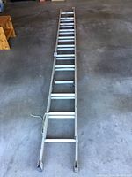 Full length image of the aluminum extension ladder laid out flat on concrete floor showing entirety and structure.