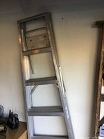 Full view of the ladder leaning against the wall, showing its three-step design and overall height.