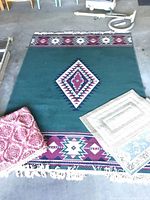 Full view of 6'x8' green geometric patterned blanket lying flat showing fringe and two smaller carpets on top