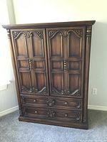 Front view of solid wood armoire showing paneled carved doors and drawers