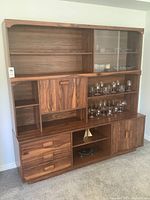 Frontal view of the wooden china cabinet and bar unit showing the varied wooden shelves, glass display cabinet on the right upper side, multiple drawers and cupboards on bottom half and open display spaces.