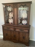 China cabinet front view showing wood finish, glass display doors with plates inside, two drawers, and four wooden doors.