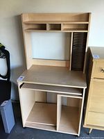 Front view showing light oak computer desk's upper storage shelves, main desk surface, side compartments, keyboard tray, and lower shelving.