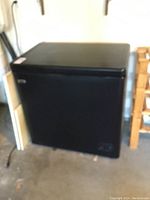 Black Danby chest freezer shown from a side angle with visible front control panel in a garage setting.
