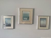 Photo showing all three framed "Dusk" prints by Peter and Traudl Markgraf hung on a wall, arranged horizontally with silver or light metallic frames and cream mats.