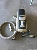 Overhead view of vintage beige Electrolux portable canister vacuum with coiled hose and two nozzle attachments on gray floor.