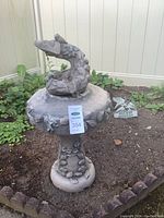 Full view of the sculpted bird bath garden feature among garden plants with Wild Bird Crossing sign behind it.