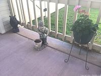 Wide view of boy planter, garden owl statue, and planter stand with plant on porch.
