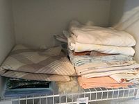Stack of folded linens including pillow cases and sheets in various colors and patterns placed on a shelf