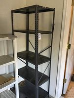 Full view of black metal storage rack with four shelves placed against a wall.