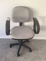 Front view of gray office chair with black armrests and black base with caster wheels.