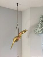 Full view of brass and copper parrot suspended from chain and ring perch.