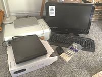Photo showing Lexmark white inkjet printer, Vizio 18-inch monitor, Logitech keyboard and mouse, Memorex DVD player on box, and pack of wooden clothespins on carpeted floor