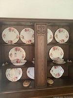 Wide view of china cabinet displaying Royal Albert American Beauty pattern dinnerware including plates, bowls, and serving pieces