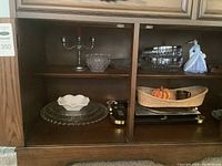 Glass and ceramic serve plates, decorative figurines, glass bowl, and metal candelabra inside cabinet.