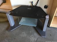Corner Sony TV stand with black top and gray legs, includes a glass shelf for VCR or media device below the top plexiglass panel