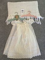 Overview of the christening gown, eyelet slip, baby hangers, and white knitted baby blanket on carpeted floor.