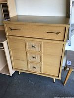 Front angled view of vintage four drawer dresser with brass handles and rattan panel middle drawers.