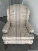 Front view of the wing back chair showing upholstery fabric with floral and striped pattern, rolled arms, and wooden legs.