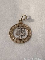 Front view of 10K gold Scales of Justice charm pendant showing detailed white gold scales centered within yellow gold circular frame with Greek key pattern and attached bail.