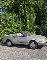 Full side view of champagne/tan Cadillac Allante with convertible top down parked on gravel.