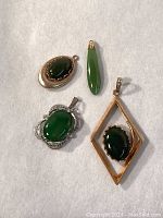 Four jade and nephrite pendants arranged on fabric background, showing various shapes and metal settings.