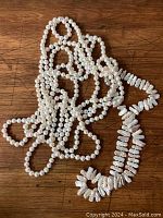 Photo shows a tangled 98" long opera-length necklace of white round freshwater pearls next to a shorter strand of stick-shaped Biwa-type pearls on wooden surface.