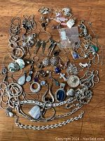 Wide view of assorted silvertone vintage jewellery including earrings, rings, bracelets, and necklaces spread on a wooden surface.