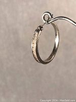 Side view of single white gold hoop earring showing channel set diamonds.